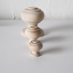 May include: Three wooden knobs of varying sizes, all unfinished and ready to be painted or stained. The knobs have a rounded top and a cylindrical base.