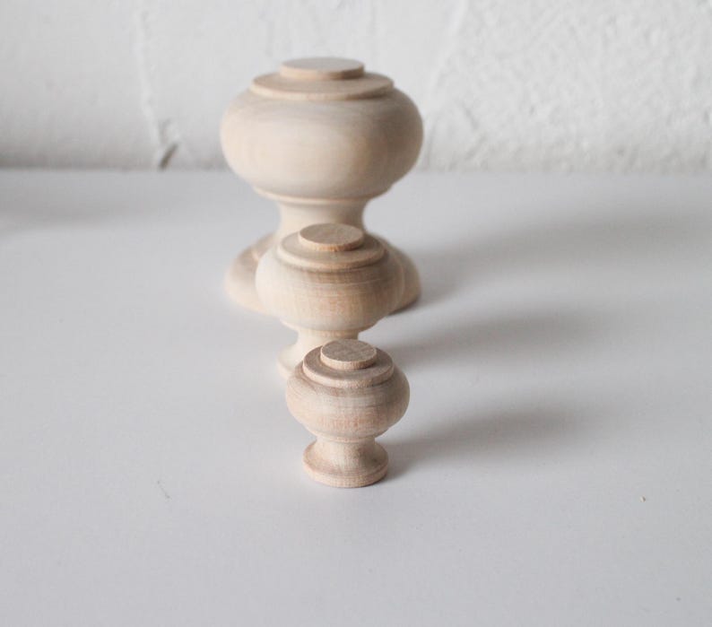 May include: Three wooden knobs of varying sizes, all unfinished and ready to be painted or stained. The knobs have a rounded top and a cylindrical base.