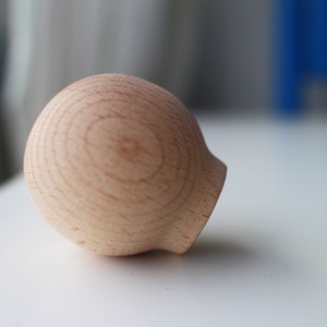 May include: A round, wooden knob with a smooth, light brown finish. The knob has a slightly rounded top and a flat bottom.