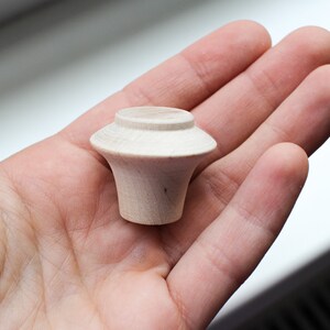 Op de afbeelding: Een kleine, onafgewerkte houten knop met een afgeronde bovenkant en een licht uitlopende basis.