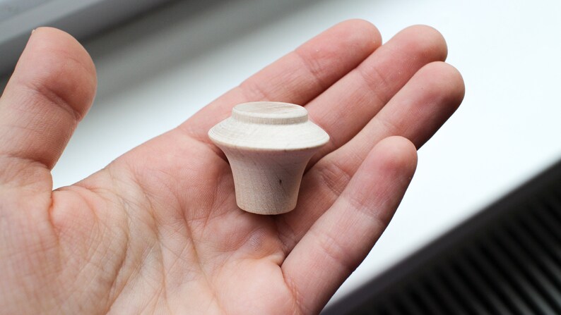 Op de afbeelding: Een kleine, onafgewerkte houten knop met een afgeronde bovenkant en een licht uitlopende basis.