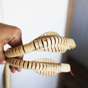 Puede incluir: Un juguete de serpiente de madera con partes del cuerpo segmentadas, hecho de madera natural. La serpiente est&aacute; enroscada y tiene dos cabezas.