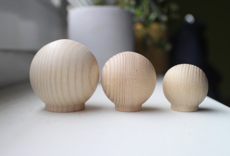 May include: Three wooden spheres of varying sizes, arranged from largest to smallest. The spheres are made of light-colored wood with a natural grain pattern.