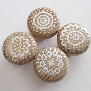 May include: Four round wooden knobs with silver painted designs. Each knob features a different geometric pattern.