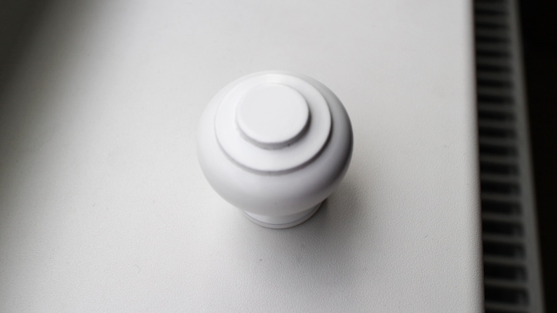 May include: White ceramic knob with a rounded top and a slightly raised rim. The knob has a smooth, glossy finish.
