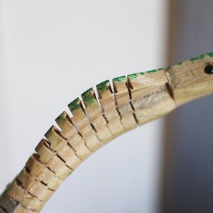 Puede incluir: Un juguete de serpiente de madera con escamas pintadas de verde y una lengua roja. La serpiente est&aacute; hecha de piezas de madera individuales que est&aacute;n conectadas entre s&iacute;.