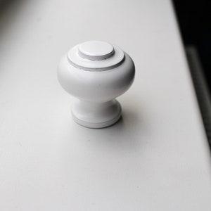 May include: White round cabinet knob with a raised centre ring.
