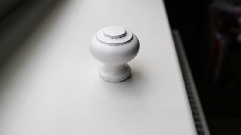May include: White round cabinet knob with a raised centre ring.