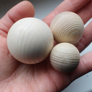 May include: Three wooden balls of varying sizes, with a natural wood grain finish. The balls are smooth and round, and they are arranged in a hand.