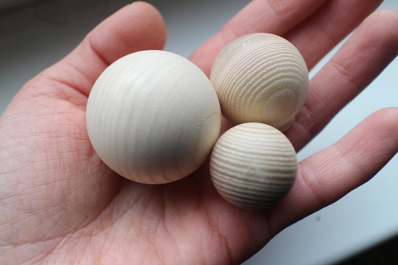 May include: Three wooden balls of varying sizes, with a natural wood grain finish. The balls are smooth and round, and they are arranged in a hand.