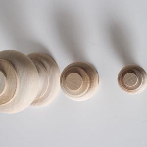 May include: Three wooden finials of varying sizes. The largest finial is a ball shape with a flat top. The other two finials are smaller and have a round top.