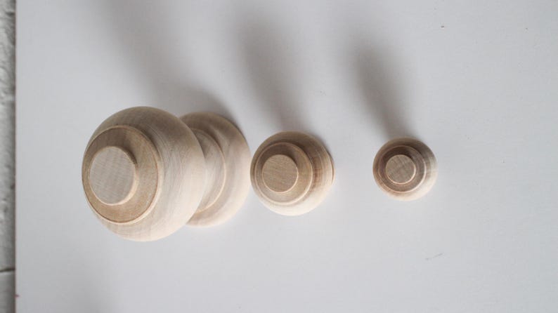 May include: Three wooden finials of varying sizes. The largest finial is a ball shape with a flat top. The other two finials are smaller and have a round top.