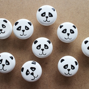 May include: Nine white round knobs with black panda bear faces painted on them.