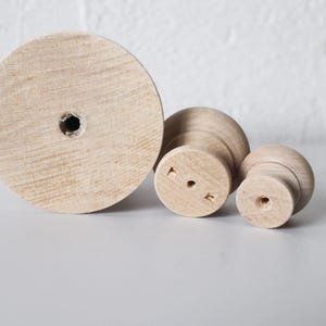 May include: Three wooden knobs of varying sizes. The largest knob is a flat circle with a hole in the centre. The other two knobs are round with a hole in the centre and a raised lip around the edge.