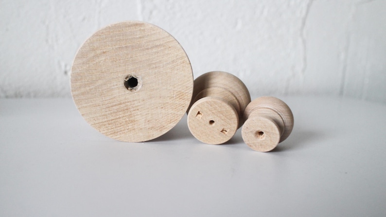 May include: Three wooden knobs of varying sizes. The largest knob is a flat circle with a hole in the centre. The other two knobs are round with a hole in the centre and a raised lip around the edge.