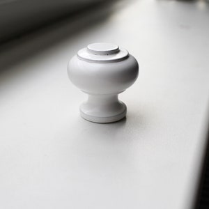 May include: White ceramic knob with a rounded top and a slightly flared base.
