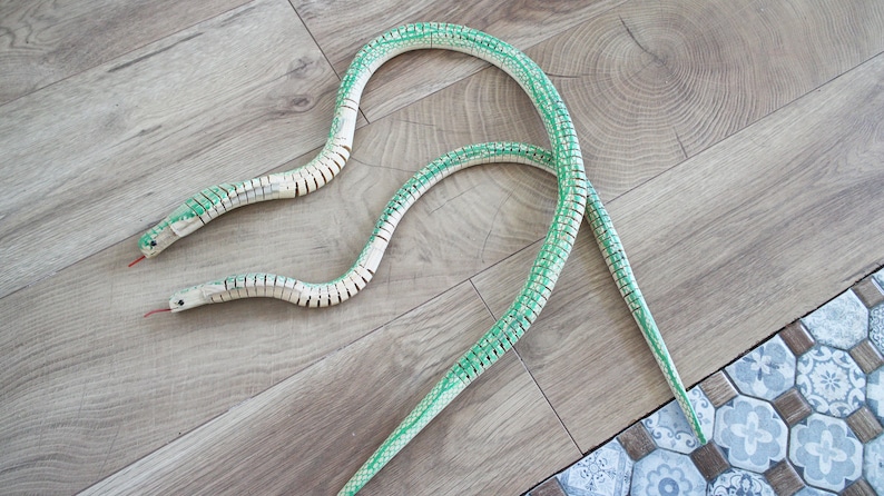 Puede incluir: Dos serpientes de juguete segmentadas de color verde y blanco sobre un suelo de madera. Las serpientes est&aacute;n hechas de pl&aacute;stico y tienen un aspecto realista.