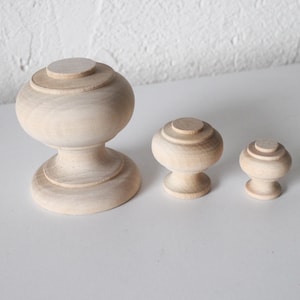 Peut inclure: Trois boutons en bois de différentes tailles. Le plus grand bouton est de forme arrondie et bulbeuse avec une base cannelée. Les deux plus petits boutons sont ronds avec un dessus cannelé.