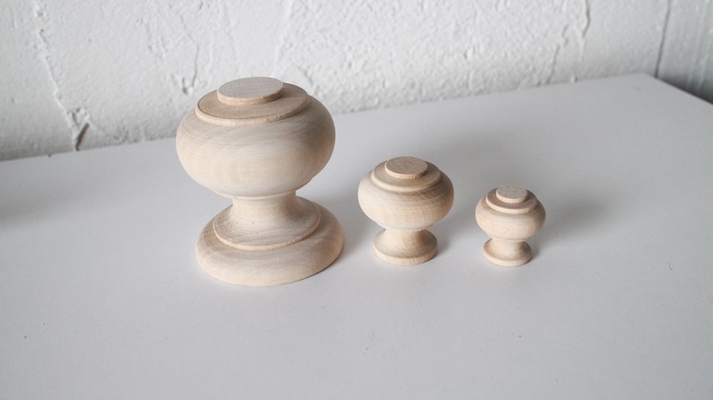 May include: Three wooden knobs of varying sizes. The largest knob is a rounded, bulbous shape with a fluted base. The two smaller knobs are round with a fluted top.