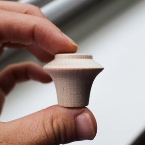 Op de afbeelding: Een kleine, onafgewerkte houten knop met een afgeronde bovenkant en een licht uitlopende basis.