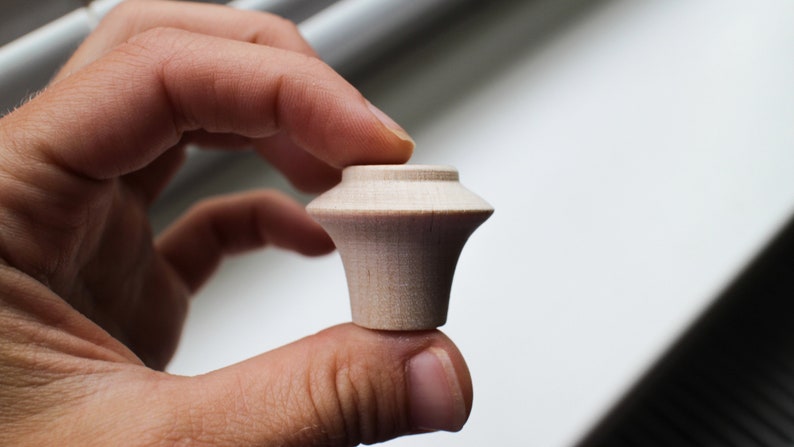 Op de afbeelding: Een kleine, onafgewerkte houten knop met een afgeronde bovenkant en een licht uitlopende basis.