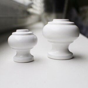 May include: Two white ceramic finials, one larger than the other, with a rounded top and a slightly flared base.