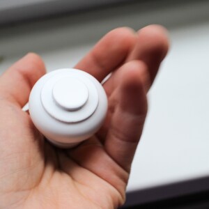 May include: White plastic knob with a circular design. The knob has a smooth, rounded surface and a slightly raised centre.
