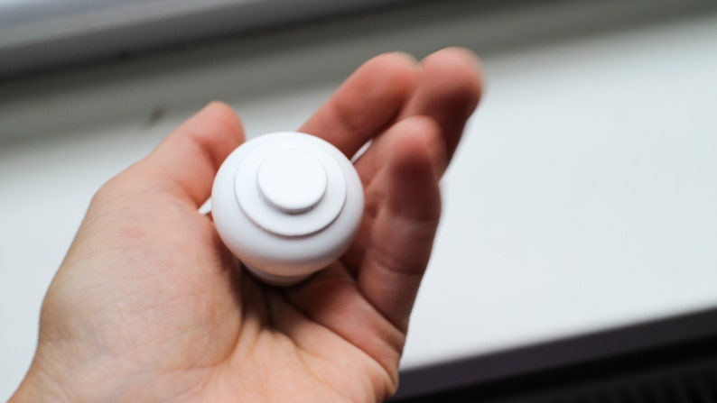 May include: White plastic knob with a circular design. The knob has a smooth, rounded surface and a slightly raised centre.