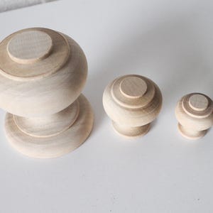 May include: Three wooden knobs of varying sizes. The largest knob is a rounded, two-tiered design. The two smaller knobs are single-tiered and round.