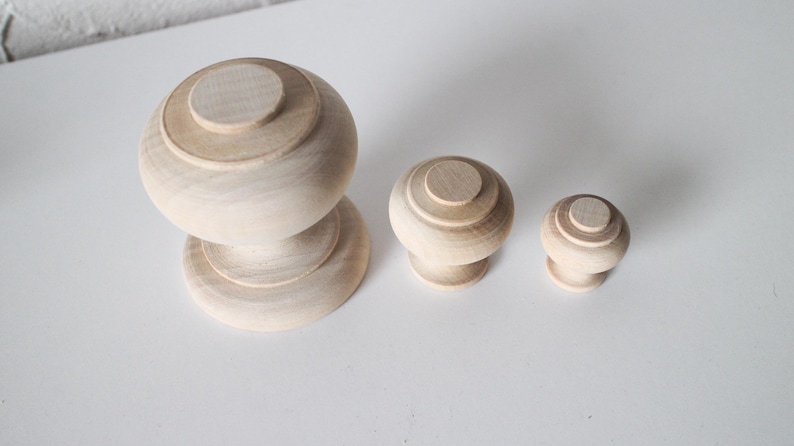 May include: Three wooden knobs of varying sizes. The largest knob is a rounded, two-tiered design. The two smaller knobs are single-tiered and round.