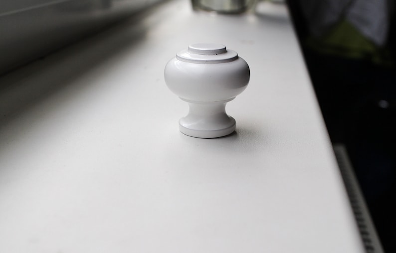 May include: White ceramic cabinet knob with a rounded top and a smooth, polished finish.