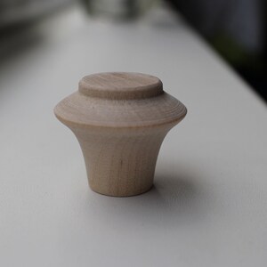Op de afbeelding: Een lichte houten knop met een afgeronde bovenkant en een uitlopende basis.