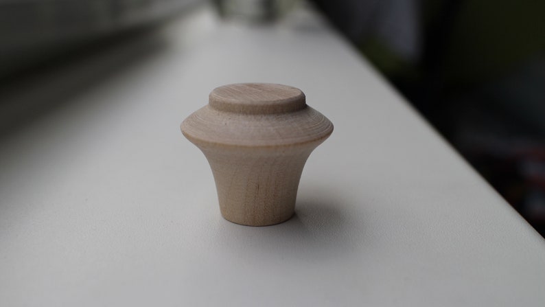 Op de afbeelding: Een lichte houten knop met een afgeronde bovenkant en een uitlopende basis.