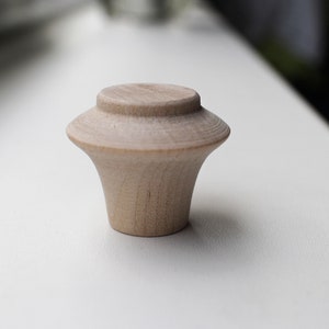 Op de afbeelding: Een lichte houten knop met een afgeronde bovenkant en een licht uitlopende basis.