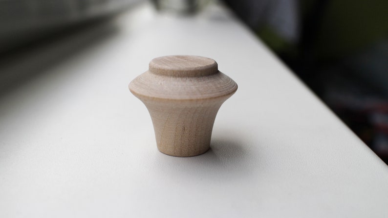 Op de afbeelding: Een lichte houten knop met een afgeronde bovenkant en een licht uitlopende basis.