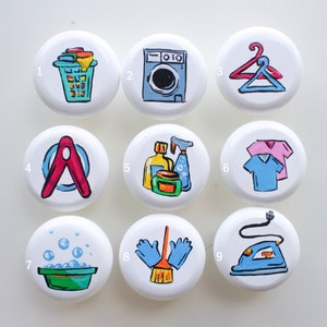 May include: Nine white round buttons with different laundry-themed illustrations. The buttons are numbered 1 through 9. The illustrations include a laundry basket, a washing machine, a hanger, a clothespin, cleaning supplies, a shirt, a bowl of soapy water, a brush and gloves, and an iron.
