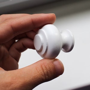 May include: White round cabinet knob with a raised centre and a small, round knob on the side.
