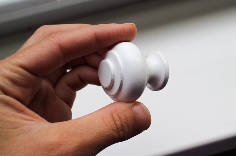 May include: White round cabinet knob with a raised centre and a small, round knob on the side.
