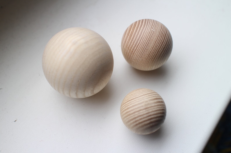 May include: Three wooden spheres of varying sizes, all with a light brown color and a wood grain pattern. The spheres are arranged on a white surface.