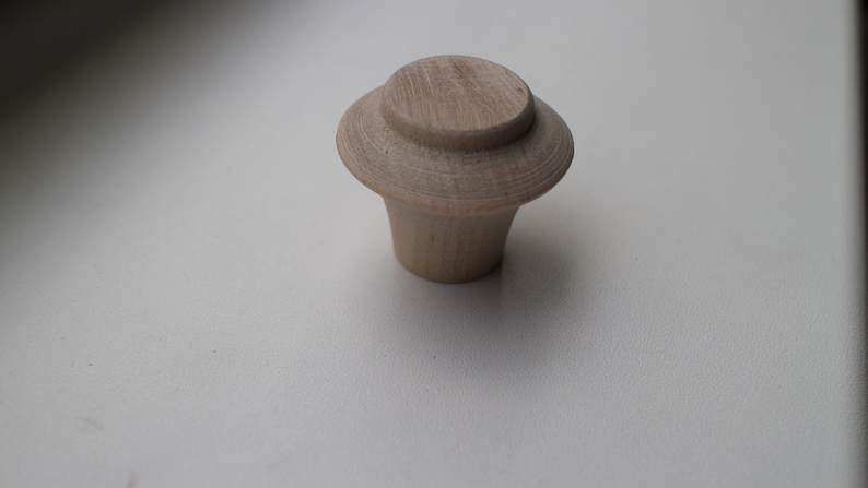 Op de afbeelding: Een houten knop met een afgeronde bovenkant en een licht uitlopende basis. De knop is lichtbruin van kleur en heeft een gladde afwerking.