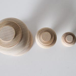May include: Three wooden nesting dolls, the largest is a light brown colour and the smallest is a darker brown. The dolls are all round and have a smooth surface.