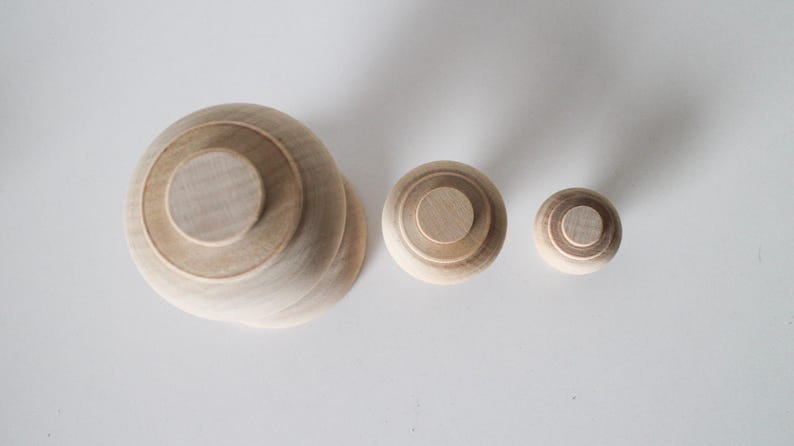 May include: Three wooden nesting dolls, the largest is a light brown colour and the smallest is a darker brown. The dolls are all round and have a smooth surface.