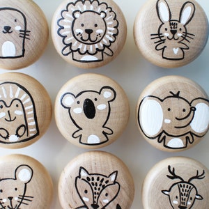 Peut inclure: Neuf boutons en bois avec des illustrations d'animaux peintes dessus. Les animaux comprennent un lion, un lapin, un éléphant, un koala, un hérisson, une souris, un renard, un cerf et une taupe.