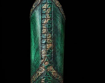 Könnte beinhalten: Ein spitz zulaufendes, zylindrisches Objekt mit einer texturierten dunkelgrünen Oberfläche. Es weist komplizierte, erhabene goldfarbene geometrische Muster und Filigrandetails entlang der Mittelachse und der oberen Kanten auf.