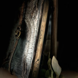 May include: A dark green leather-bound journal with a silver and gold embossed design. The journal is closed and has a metal clasp.