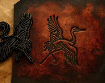 May include: Close-up of a leather craft featuring a crane design. The image shows a black crane cutout and a crane embossed on a reddish-brown leather surface. The background is a lighter brown.