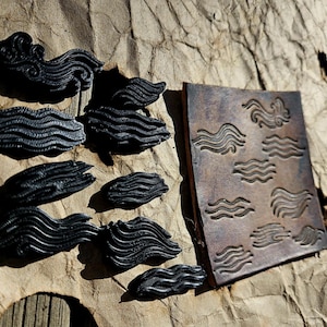May include: Black leather craft items, including wave-shaped cutouts and a rectangular piece with wave patterns. The items are arranged on a textured, brown surface, suggesting a leather craft theme.
