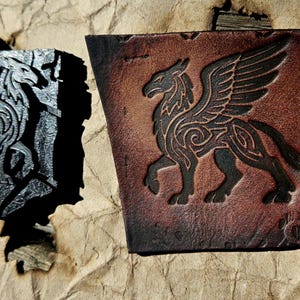 May include: Two leather squares with embossed griffin designs. One is dark grey, the other is brown with black detailing. The griffin is a mythical creature with the body of a lion and the head and wings of an eagle.
