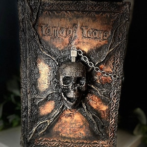 May include: A dark brown leather-bound book with a skull and chain design. The book is titled "Tome of Tears".