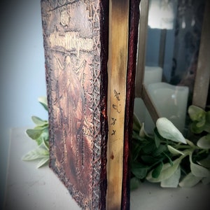 May include: A brown leather-bound journal with embossed details and a gold spine. The journal has the title "The Witches'  Manuscript" on the front cover.